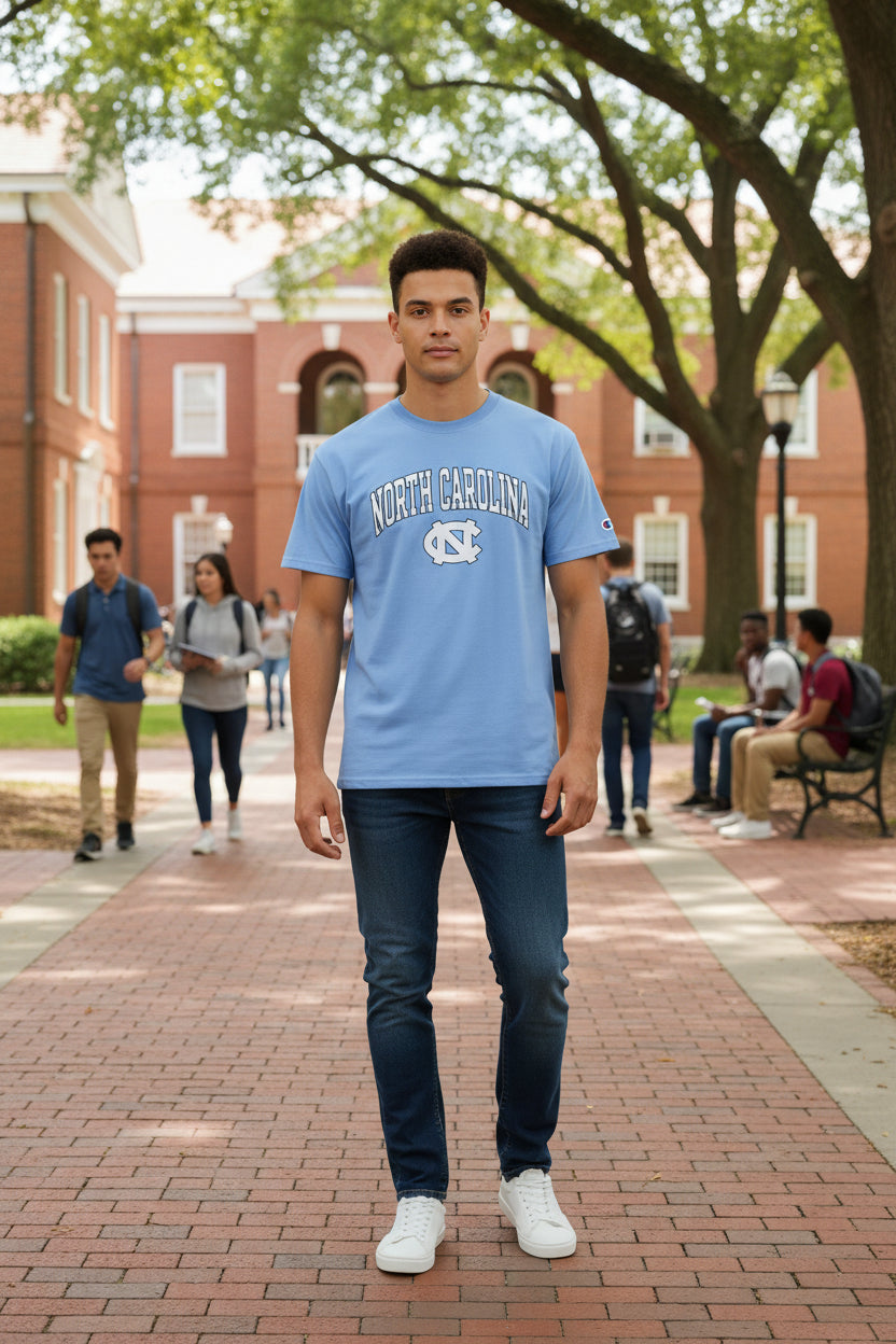 A light blue short-sleeve t-shirt with 'NORTH CAROLINA' and the NC logo printed in white and dark blue on the chest. A small Champion logo is visible on the left sleeve.